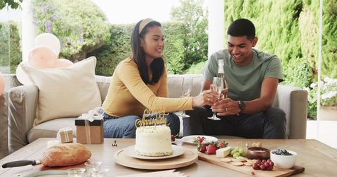 Young couple celebrating anniversary outdoors with cake and champagne
