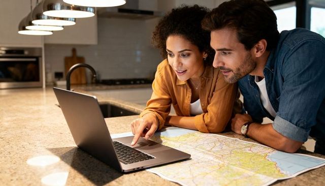 Couple planning road trip at granite kitchen island with laptop and unfolded paper map