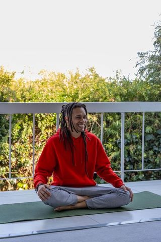 African american man sitting cross-legged on balcony practicing yoga and smiling