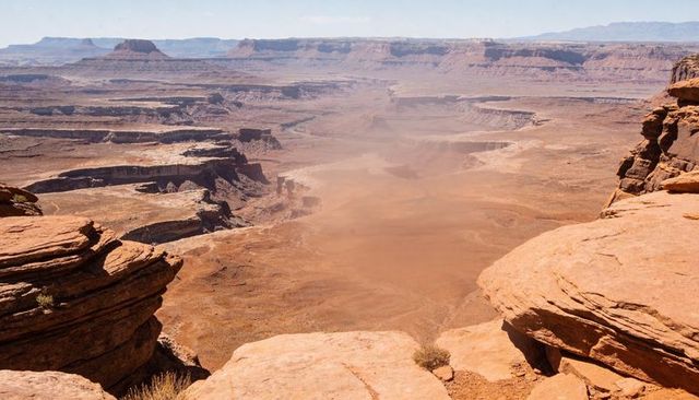 Aerial canyon overlook showcasing layered sandstone mesas and dust-filled desert valley