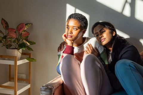 Sunlit intimate moment between black woman and south asian partner on minimalist sofa
