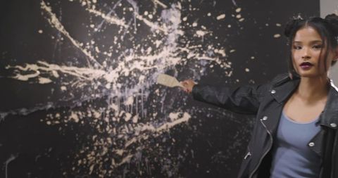 Asian woman applying paint with palette knife on large abstract splatter canvas