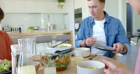 Family sharing casual dinner at modern kitchen island, passing plates and serving salad
