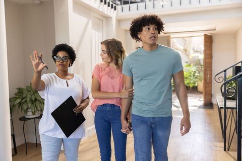African american agent touring sunlit foyer with young couple holding hands home showing