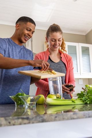 Smiling multiracial couple preparing green smoothie together in modern kitchen
