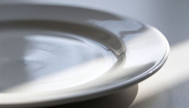 Glossy white ceramic dinner plate catching soft sunlight on light tabletop