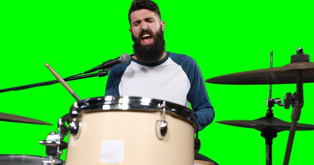 Man passionately singing and playing drums in front of green screen. Great for music-related content, promotions for music equipment, illustrating concepts of creativity and expression, or advertisements for live performances.