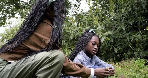 African American mother and daughter exploring garden, examining yellow flower together