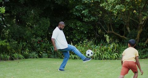African american father playing soccer with son on backyard lawn for family playtime