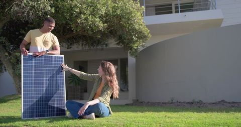 Diverse couple installing solar panel on lawn of modern suburban home