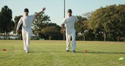 Two diverse cricketers walking and gesturing during sunlit practice with training cones