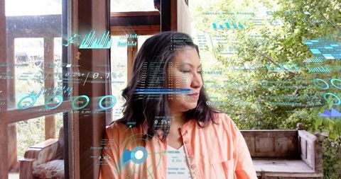 Mature woman standing on porch studying holographic data overlays with garden backdrop