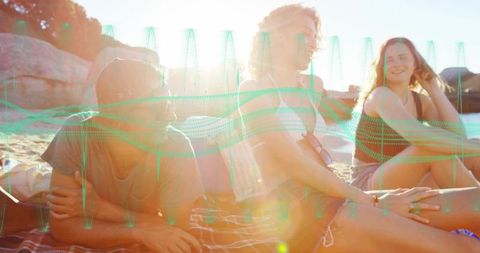 Friends relaxing on sunlit beach at golden hour with lens flare and striped blanket