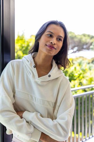 African american woman leaning in doorway wearing white hoodie overlooking sunlit balcony