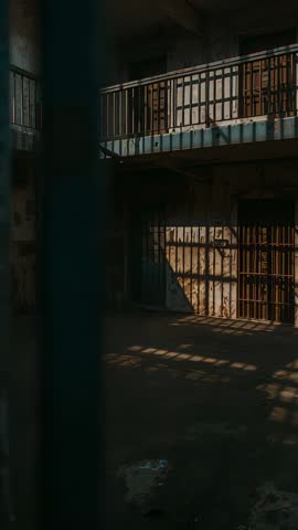 Vertical video showing sunlight shifting across abandoned prison cellblock, rusted bars