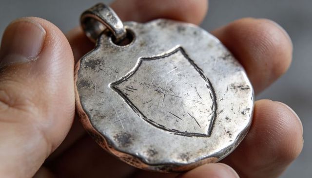 Worn silver shield pendant held in hand macro closeup engraved medallion with patina