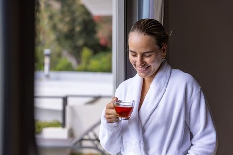 Balcony morning ritual, woman in white robe enjoying hot tea and quiet daylight
