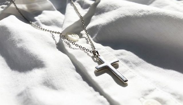 Resting silver cross pendant on white shirt front catching sunlight and casting shadow