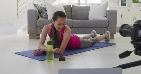 Korean woman exercising on yoga mat at home filming fitness tutorial for social media