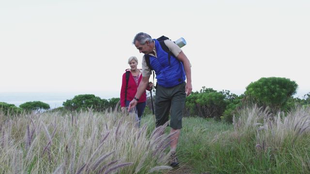 Senior couple enjoying a hike in natural surroundings, touching grass as they walk along a path. Great for themes related to healthy retirement, active lifestyle, outdoor activities, natural exploration, and bonding in nature.