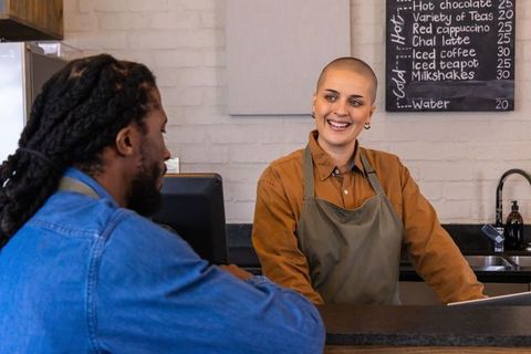 Friendly barista with shaved head talking to african american customer at cafe counter