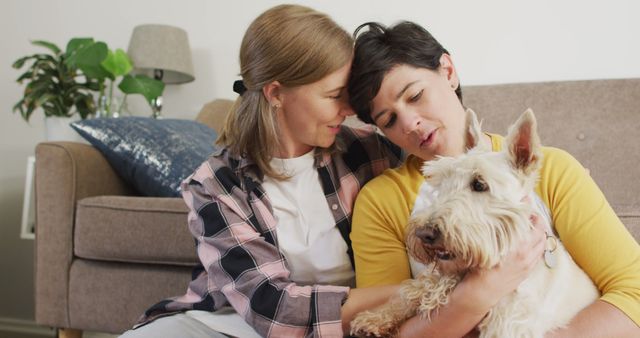 Caucasian woman kissing her wife on forehead while she plays with her dog at home. lgbt relationship and lifestyle concept