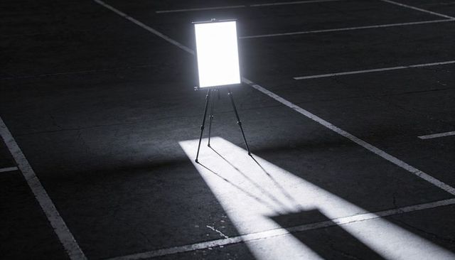 Led panel on tripod casting light beam and long shadow across dark parking lot