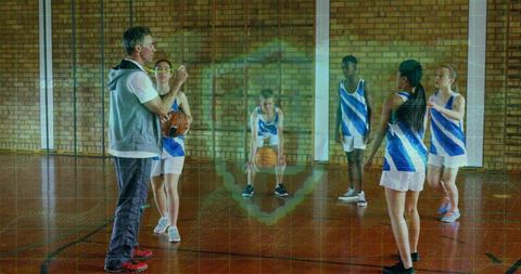 Coaching youth basketball team during drills on indoor hardwood court with brick wall backdrop