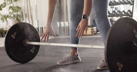Close-up athlete gripping barbell for deadlift with chalk dust rising on gym floor