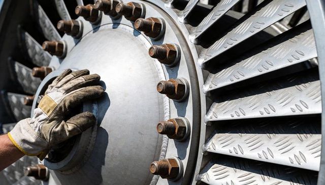 Resting gloved hand touching turbine hub displaying rusted bolts and diamond-plate blades