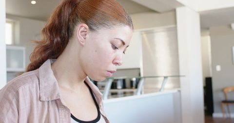 Contemplative black woman gazing in modern kitchen wearing beige overshirt and ponytail