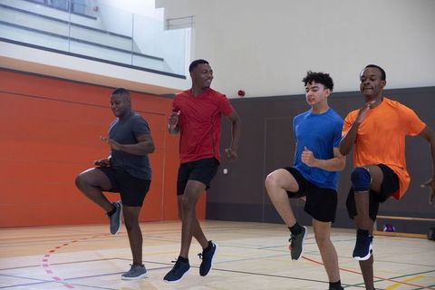 Diverse male athletes performing high-knee agility drills in school gym for team training