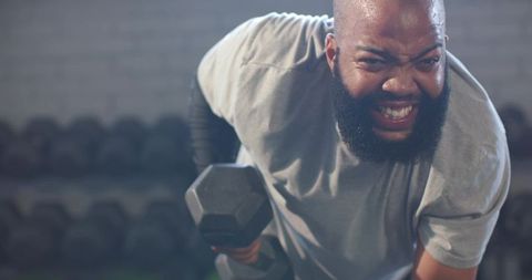 African American man lifting heavy hex dumbbell gritting teeth during intense gym row
