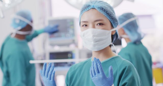 Image portrait of asian female surgeon in cap, gloves and face mask in operating theatre, copy space. Hospital, medical and healthcare services.