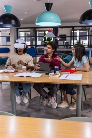 Diverse students collaborating with vr headset and tablet in modern co-working workspace