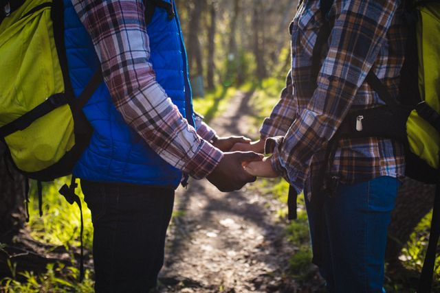 Mid section of couple holding hands while trekking in the forest. trekking, adventure and travel concept