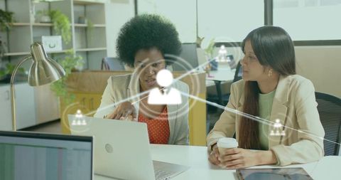 Two Professional Women Collaborating Over Laptop with Network Overlay in Modern Workspace