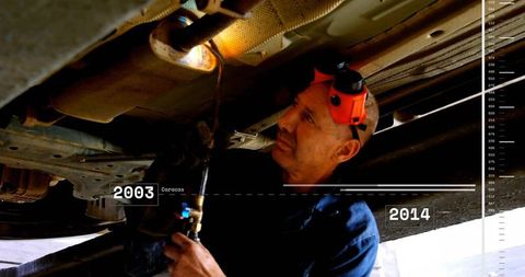 Mechanic heating undercarriage with torch while inspecting underbody in auto repair bay