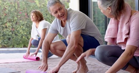 Senior Friends Unrolling Yoga Mats by Poolside