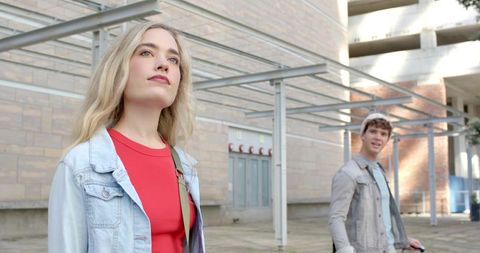 Young couple walking sunlit urban plaza with scooter and denim jackets