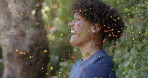 Smiling young man wearing blue t-shirt standing in garden with colorful particle overlay