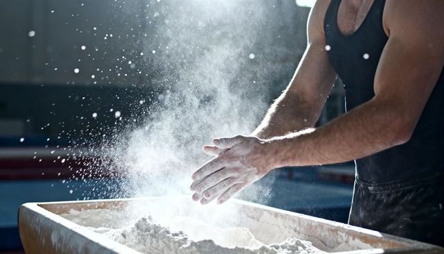 Muscular athlete clapping chalked hands over gym chalk tray, powder cloud backlit