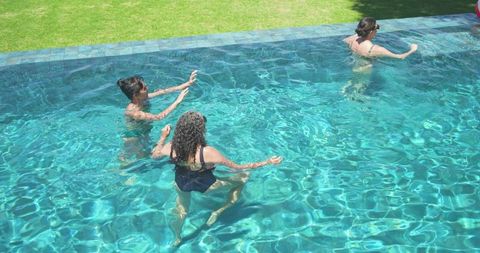 Wading women in turquoise backyard pool enjoying sunny swim and friendship