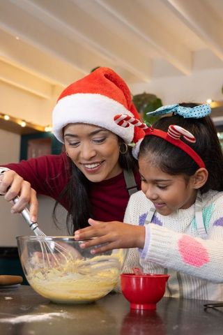 Asian mother and daughter mixing holiday batter in kitchen wearing santa hat and candy-cane headband
