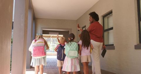 African american teacher leading group of elementary students down sunlit school corridor
