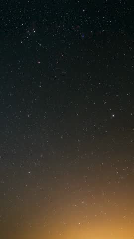 Vertical night sky video showing meteors streaking over warm glowing horizon at dusk