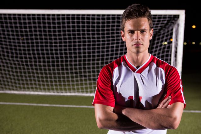 Portrait of confident young male soccer player standing with arms crossed against goal post on playing field