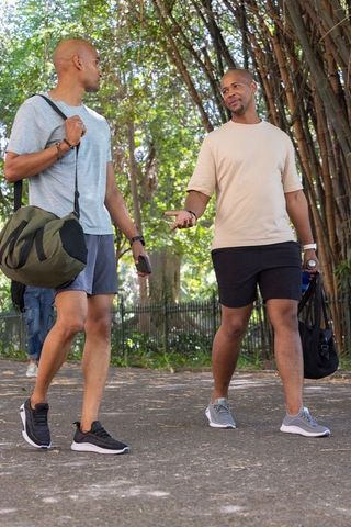 African american friends walking in park carrying duffel bags and chatting in activewear