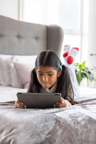Young asian girl lying on bed using tablet with red polka dot socks for home learning