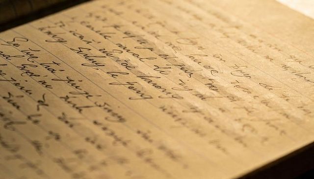 Vintage yellowed ruled page with cursive handwriting under warm desk lamp closeup